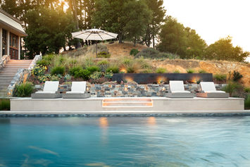 Montana stone veneer seat wall and linear fire feature seen across the pool at sunset