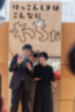 「けっこんしきはこんなにわちが」と書かれた京都の結婚式パネルの前で微笑む男女
