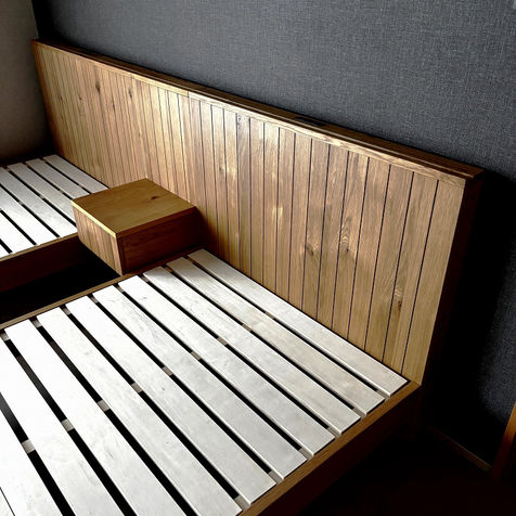 2台のシングルベッドとスモールキャビネットを写したベッドルームのディテール写真。ヘッドボードにスマホスタンド付き。