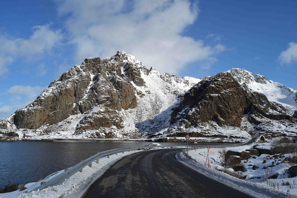 strada che conduce all'abitato di Henningsvær alle isole Lofoten, con montagne innevate e acque calme sul fiordo durante una giornata soleggiata