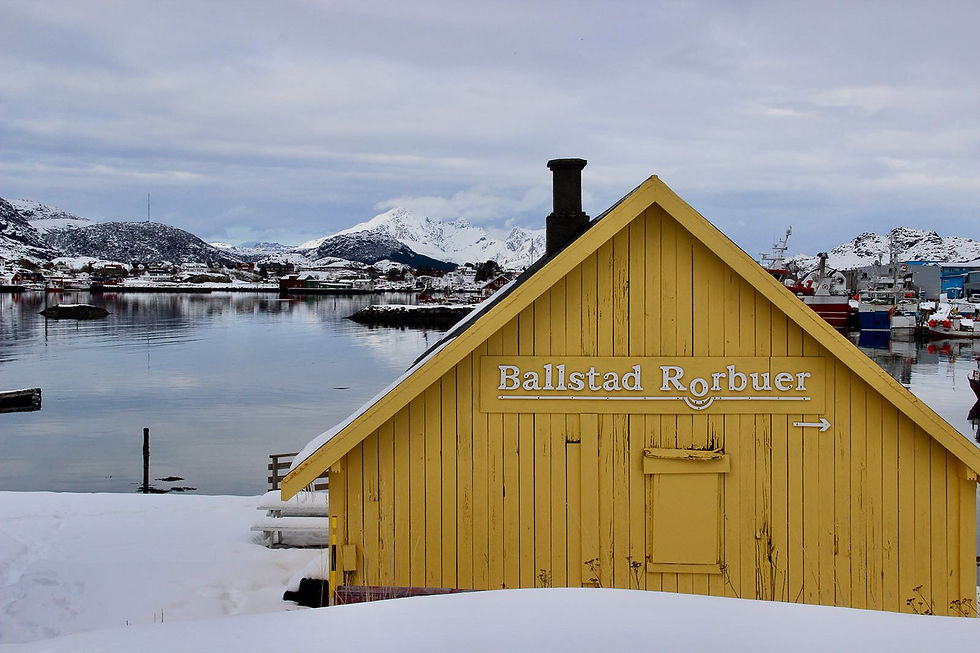 Tipica costruzione in legno colorato delle isole Lofoten nel villaggio di Ballstad, con acque calme del fiordo sullo sfondo e montagne innevate