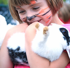 Child with tiger face paint hugging a rabbit