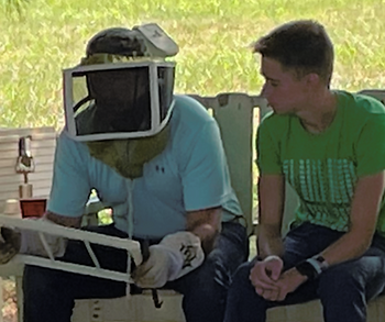 Two men, one in beekeeping gear.