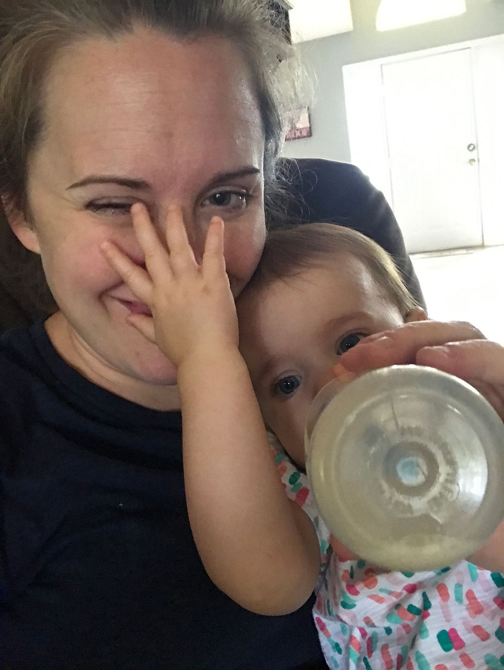 A mom with her baby drinking from a bottle and smooshing her face with one hand