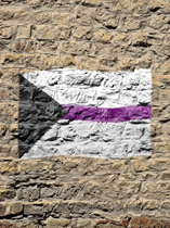 Demisexual flag with black triangle on its side on the left, white and grey blocks and a purple line in the middle painted on a stone wall