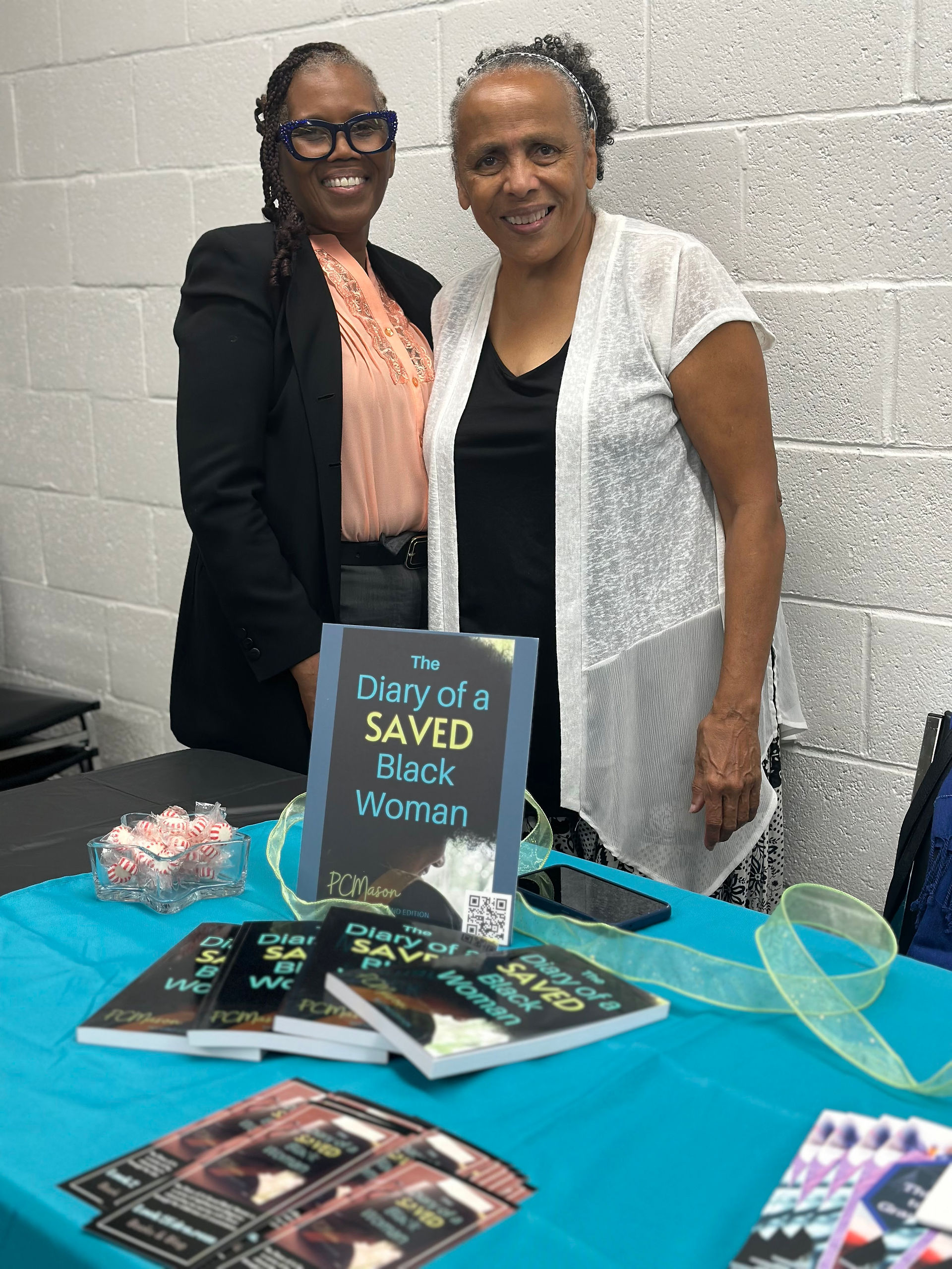 Pam Mason and another woman standing behind the table display of "The Diary of a SAVED Black Woman"