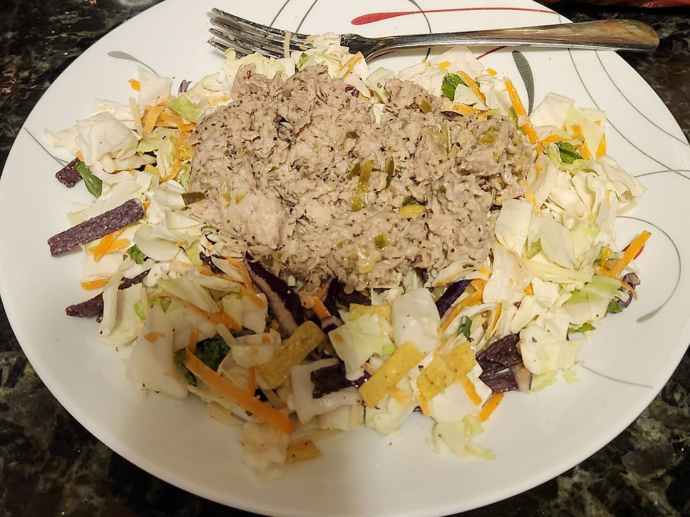 A plate with a tuna salad on a bed of mixed greens, cabbage, and tortilla strips. A fork rests on the edge. The background is a dark marbled surface.