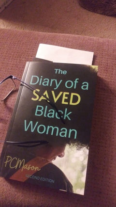 Picture of the book, The Diary of a Saved Black Woman, on a cushion with a pair of reading glasses laid to the side.
