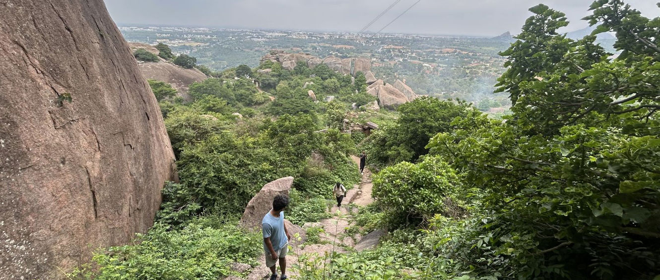 Trekkers heading down a stone path through green scrub, with the plains spread out below