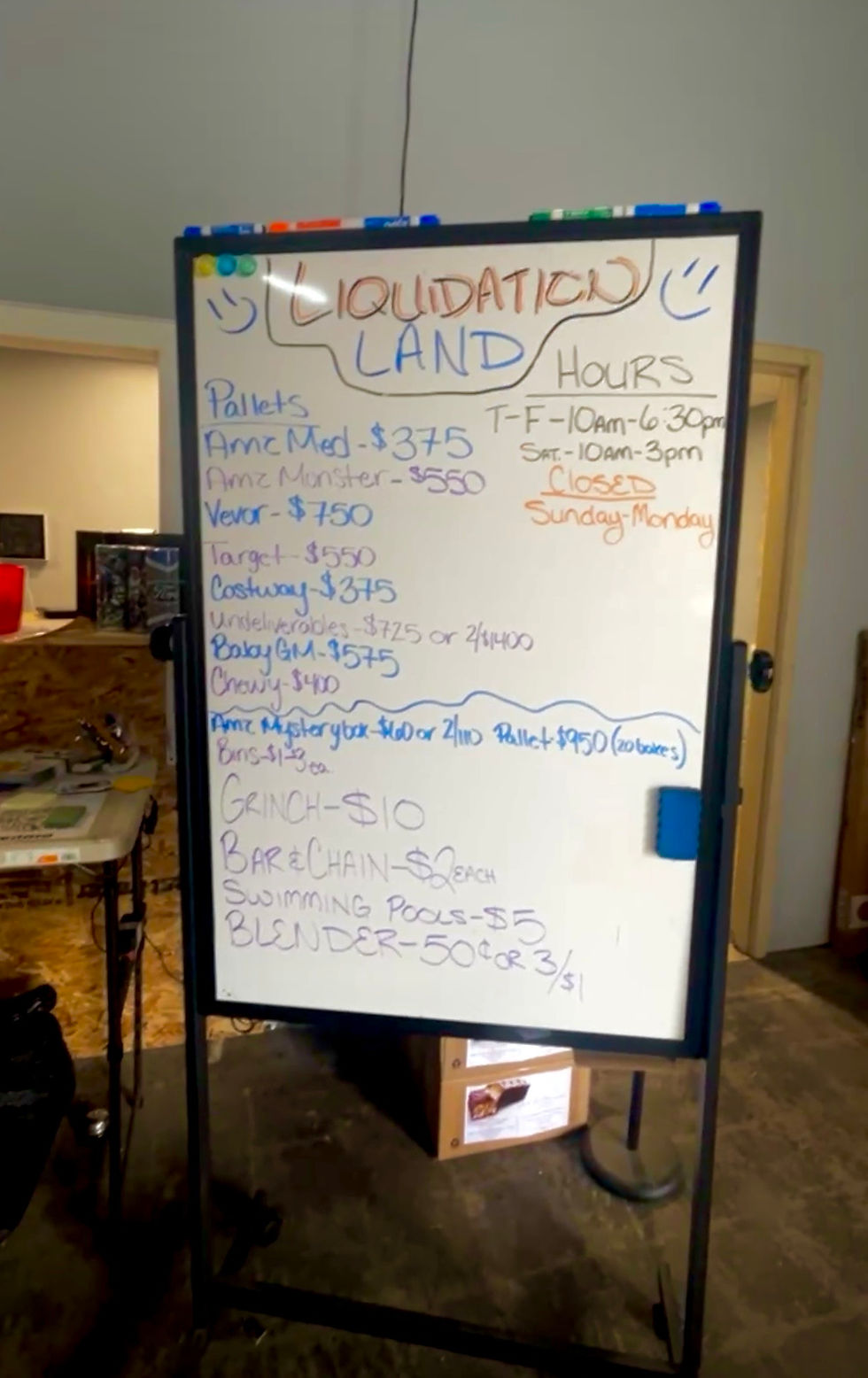 This is a whiteboard at Liquidation Land that has the deals written out on it. There are also hours for this week showing the business is closed for the 4th of July holiday.