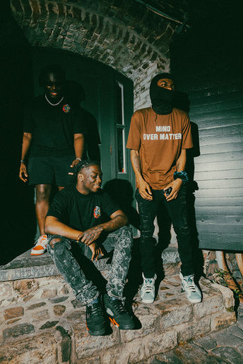 Three men pose on stone steps, one in HOME OVER MATTER shirt.