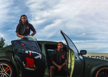 Two people pose with custom green car featuring red logo and monster graphic.