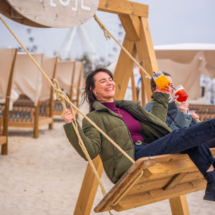 Eine Schaukel am Strand mit zwei Frauen mit Cocktails in der Hand, eine Beachbar in Grömitz an der Ostsee.