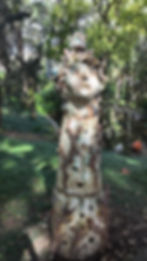 A sculpture of a women's head covered in different flowers, leaves and tree branches posted on top of a tree.