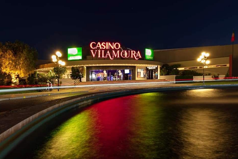 Casino Vilamoura lit up at night with colorful reflections on water. Neon signs glow in a lively setting, creating a vibrant mood.