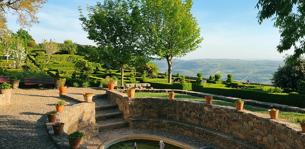 Serene garden with terraced hedges and potted plants, stone path and bench, overlooking distant hills under a clear blue sky.