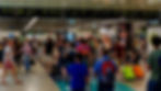 Crowded airport terminal with travelers, luggage, and overhead signage in multiple languages. Vibrant atmosphere with colorful bags.