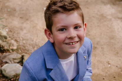 jongen in een blauw kostuum tijdens zijn communieshoot in de canna banana in putte, naar boven kijkend, lachend