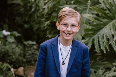 Tienerjongen in een blauw kostuum tijdens communiefotoshoot in de canna banana in Putte, al lachend