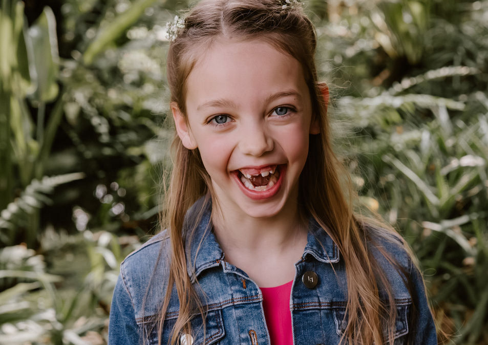 toffe foto van een communiesessie, een meisje dat heel hard lacht tussen de planten
