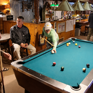 Two guests playing a game of pool on the green felt billiard table inside the rustic VC Tavern at Lee's Ferry Lodge