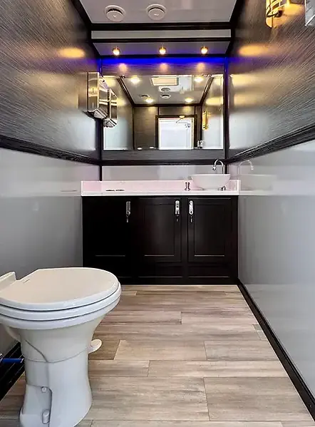 Restroom trailer interior with a flushing toilet, sink vanity, mirror and overhead lighting