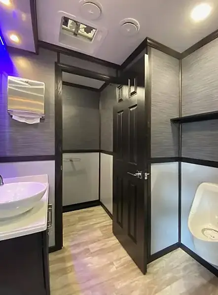Restroom trailer interior with a sink, paper towel dispenser, urinal and private toilet stall