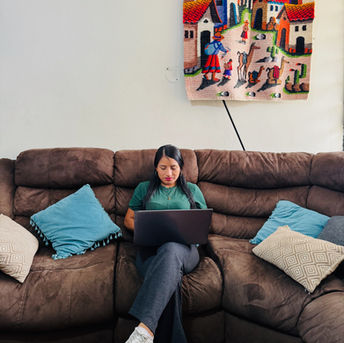 Woman working on laptop sitting on brown sofa in living room