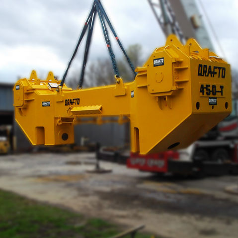 Heavy yellow DRAFTO 450-T lifting beam suspended by crane cables.