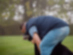 Man in blue vest hugs black dog on grassy field, foggy background. The mood is affectionate and serene.