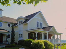 A classic, light yellow, custom New England-style home with white trim sits on a sun-lit lakefront hillside in NH.