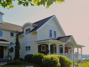 A classic, light yellow, custom New England-style home with white trim sits on a sun-lit lakefront hillside in NH.