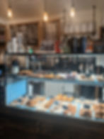 Bakery display with assorted pastries under warm lighting. Signs read "Fresh Baked Pastries Daily" and "Cold Spring Coffeehouse Travel Cups."