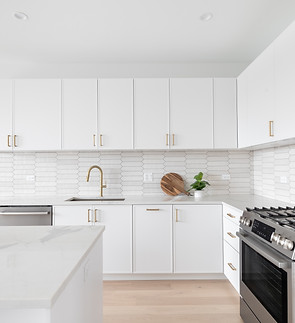 A beautiful kitchen detail with white cabinets, a gold faucet, white marble countertops, a