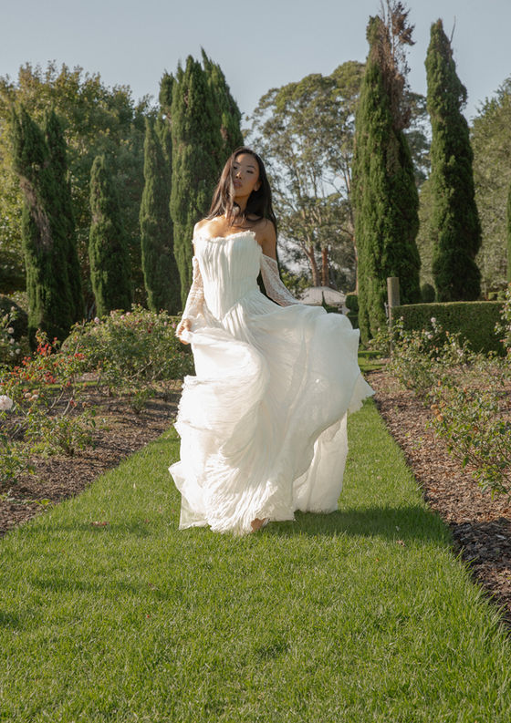 ASTON Harper Gown featuring hand pleated silk georgette with a soft scoop neckline and modern square basqued waist detail. The subtle lace detailing under the layers of hand pleated silk georgette and semi sheer design creates a soft and dreamy feel.