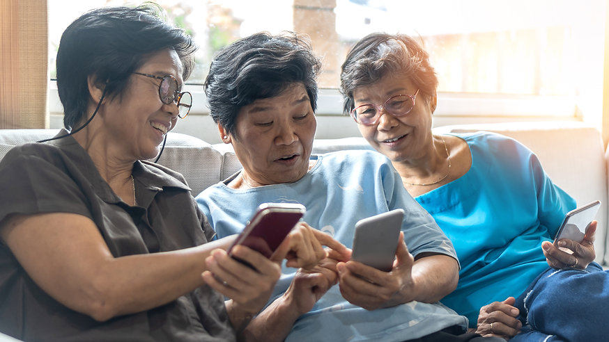 Three older women of Asian heritage sitting on a couch and reading messages on a smart phone