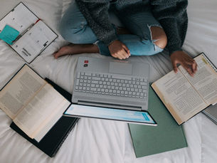 student on their bed with a notebook, 2 books and a laptop open - studying