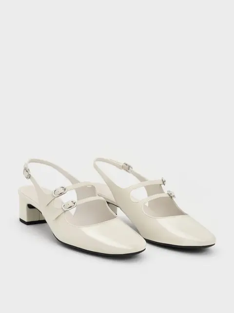Cream slingback shoes with shiny finish, two silver buckles, and low block heels, set against a plain white background.