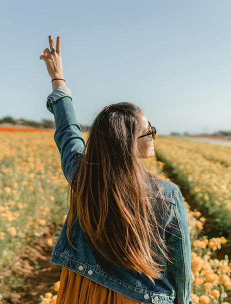 White woman in a field of flowers raising her hand in a peace sign