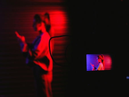 Woman bathed in red light looking at a screen while another screen tapes her.