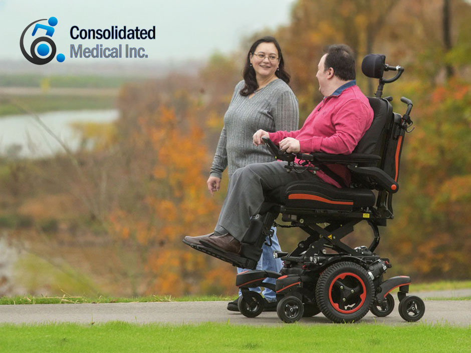 A friendly couple talking as they stroll a wooded paved path, one walking and one in a complex wheelchair.