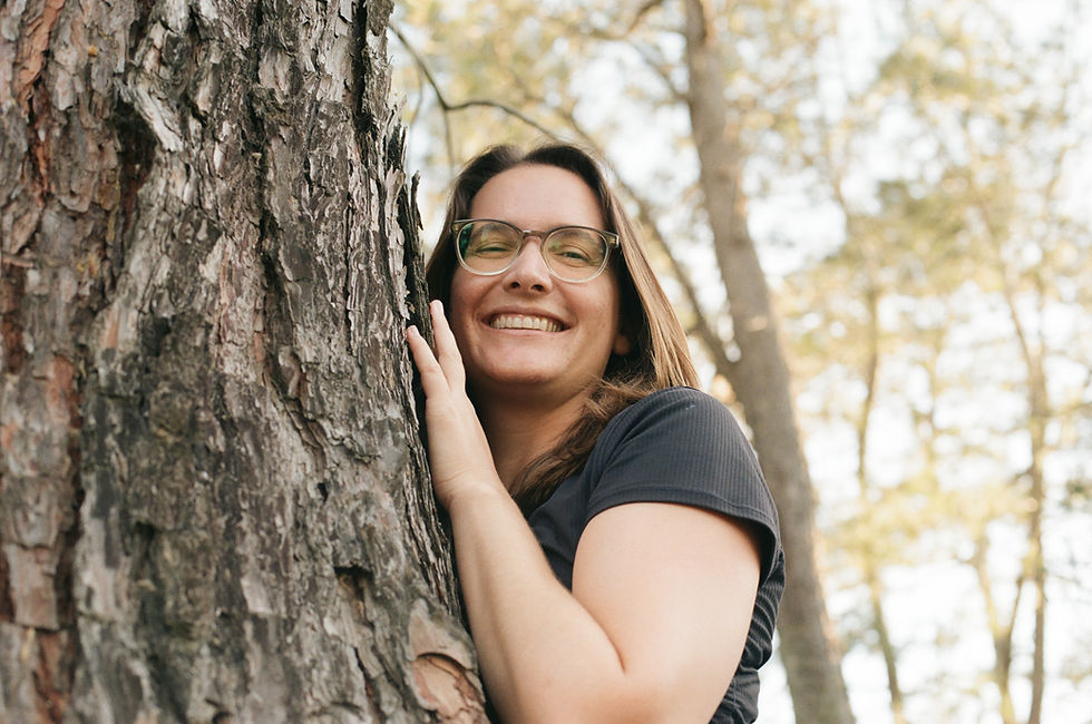 Woman in glasses smiling, hugging a tree