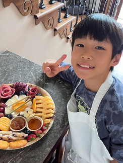a male student from itty bitty bakers stands proudly with his completed charcuterie board