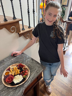a female student from itty bitty bakers stands proudly with his completed charcuterie board