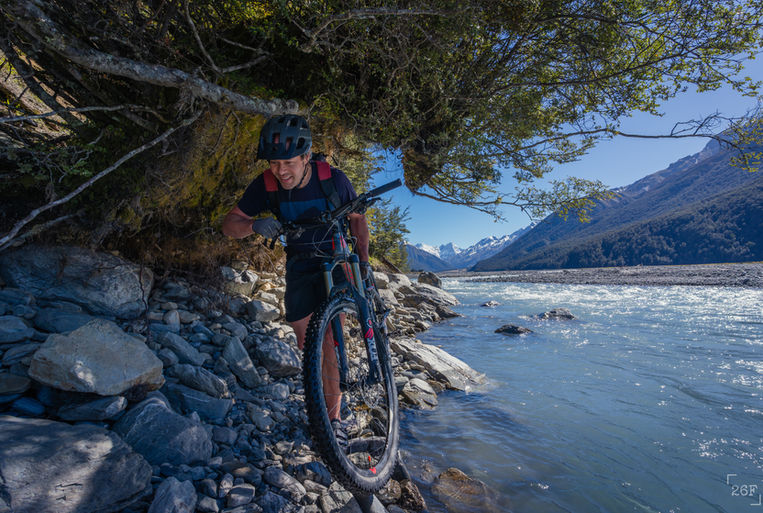 Mountain biker carrying bike along trail next to Hopkins River, in the Canterbury High Country