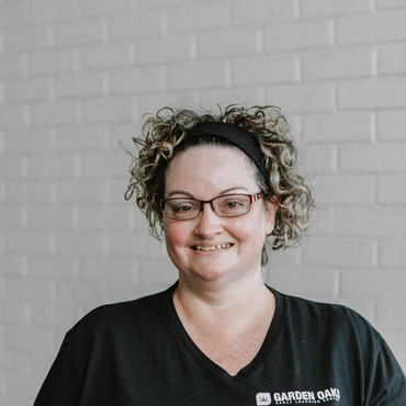 Smiling female preschool teacher poses in white brick hallway at early learning center in Houston, TX.