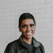 Young smiling preschool teacher poses in white brick hallway at early learning center in Houston, TX.