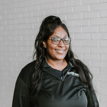 Young preschool teacher smiles at camera; posing in white brick hallway at early learning center in Houston, TX.