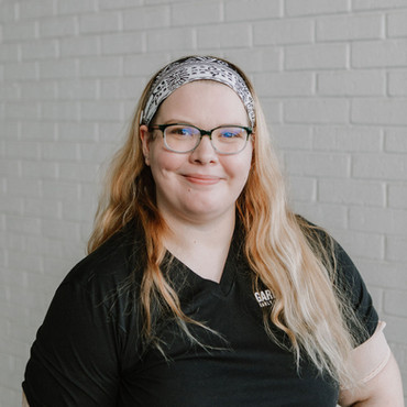 Young blonde woman in black t-shirt poses in white brick hallway at early learning center in Houston, TX.