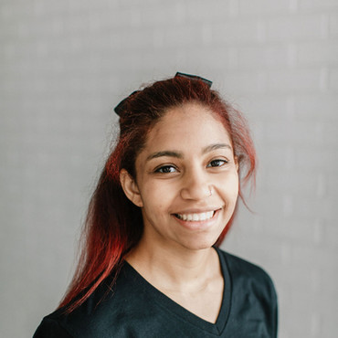 Young female preschool teacher in black shirt with ELC logo poses in white brick hallway at early learning center in Houston, TX.